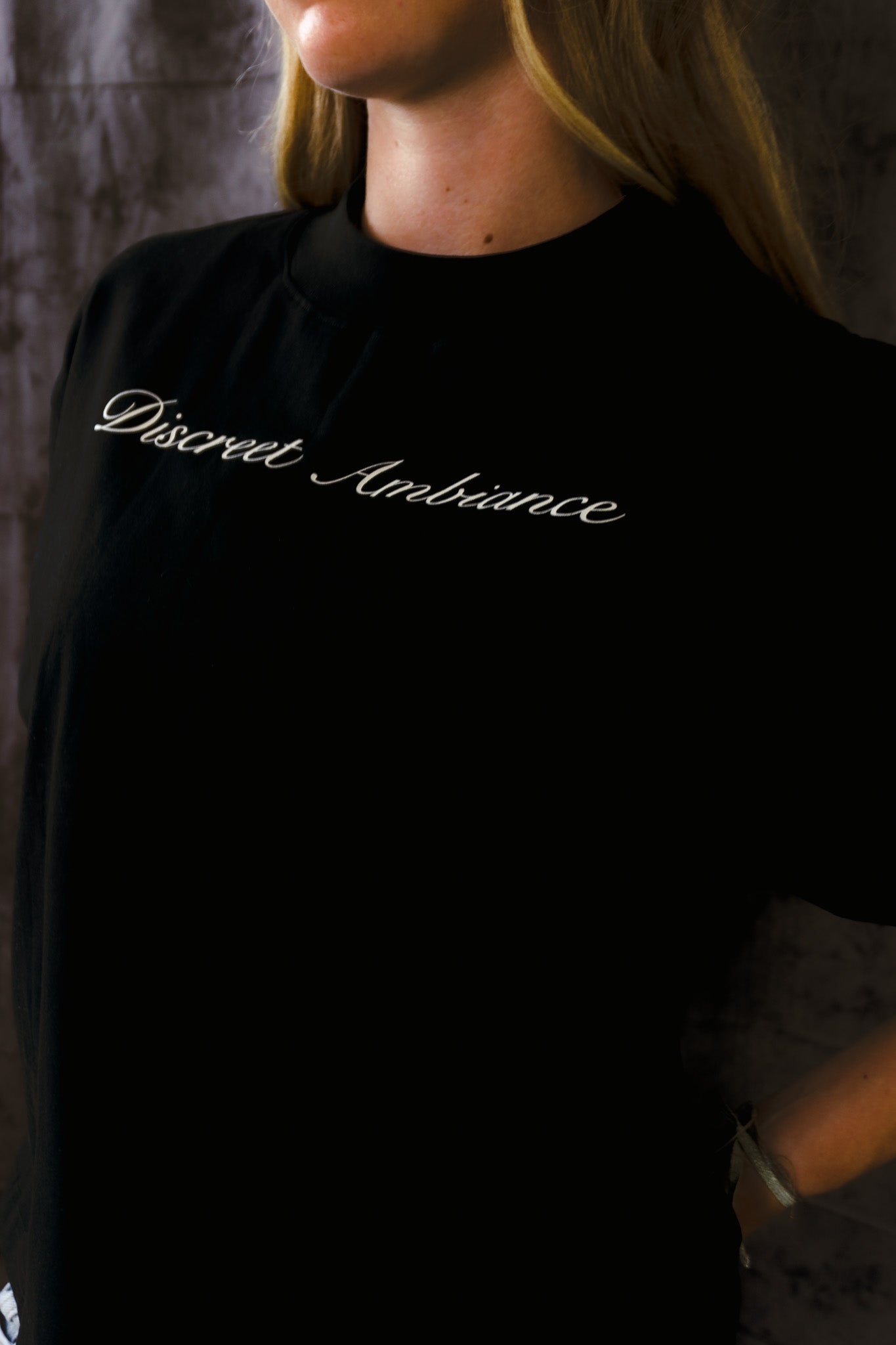 Person wearing a black shirt with 'Discreet Ambiance' text against a textured wall.